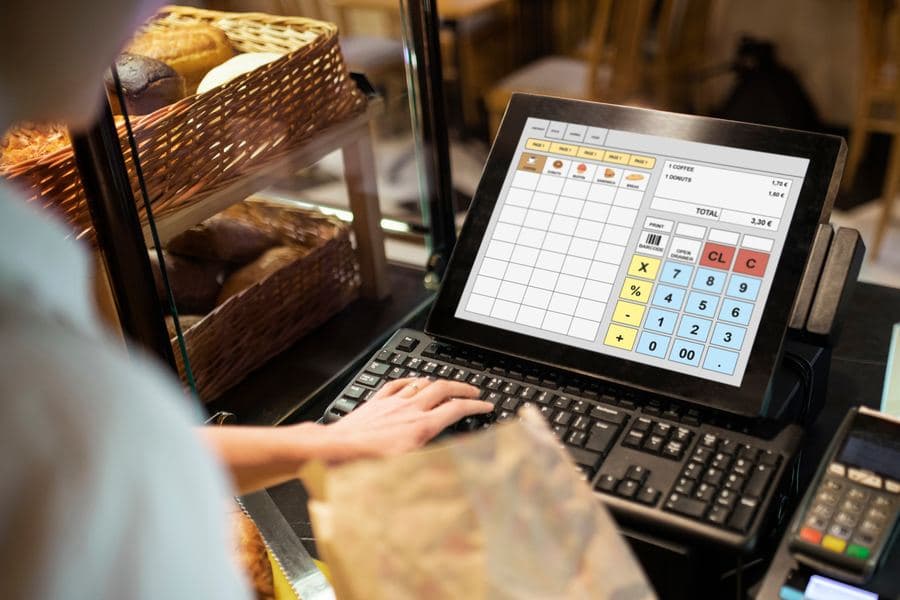 Bakery cashier keying an order into a countertop touchscreen till beside trays of bread
