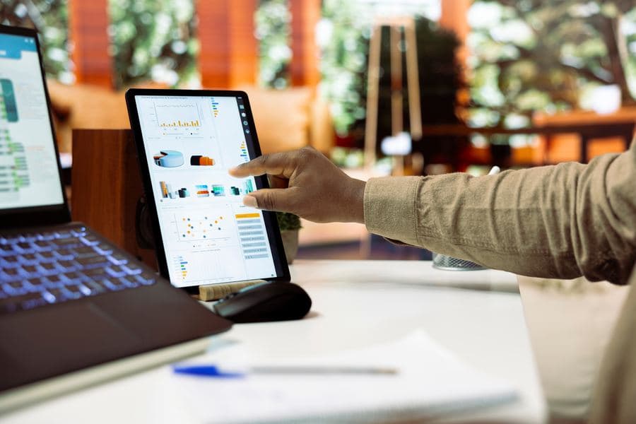 Hand pointing at a dashboard of charts on a tablet propped up on a desk