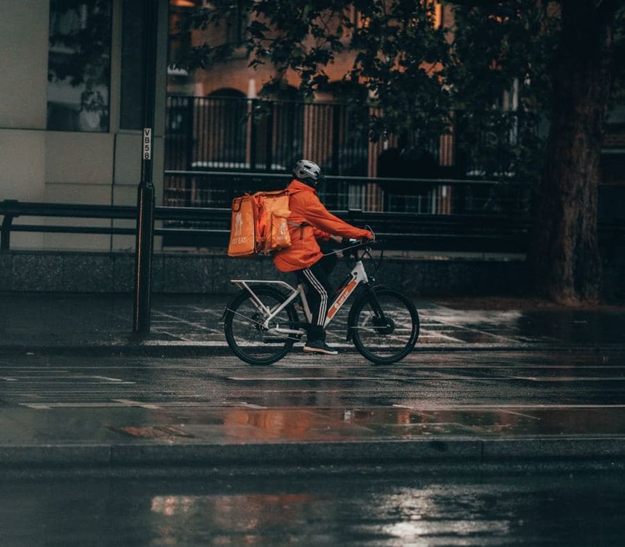 Courier cycling along a wet city street with an insulated delivery box on their back