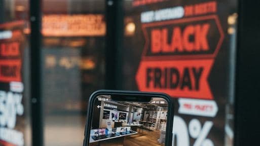 Shopper holding a phone up to a shop window covered in sale posters