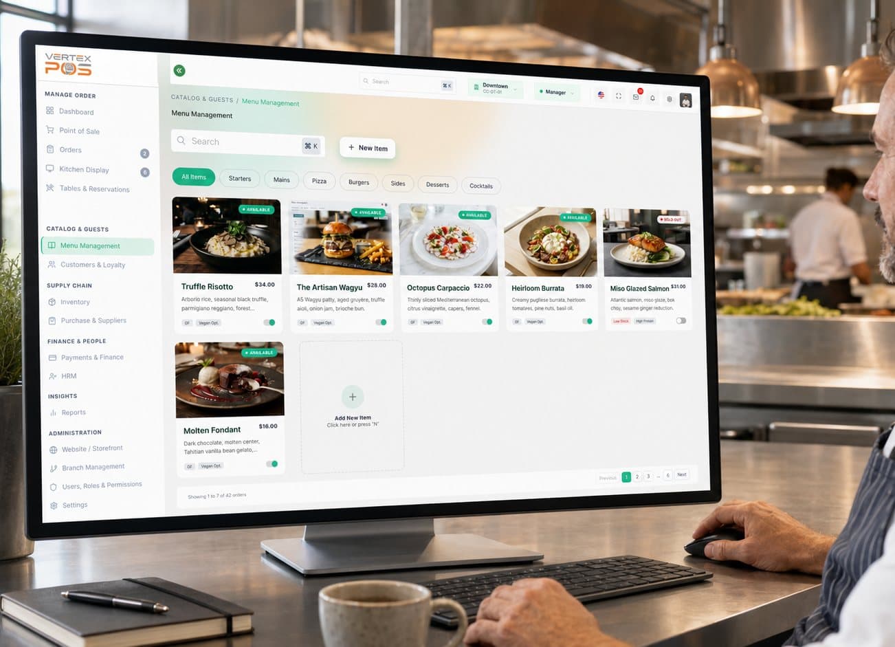 A manager working in the Vertex POS Menu Management workspace on a desktop monitor in a restaurant kitchen. The catalog grid shows each dish with its photo, name, price, short description, an availability toggle and the dietary tags the operator has entered, next to category filters and an Add New Item tile.