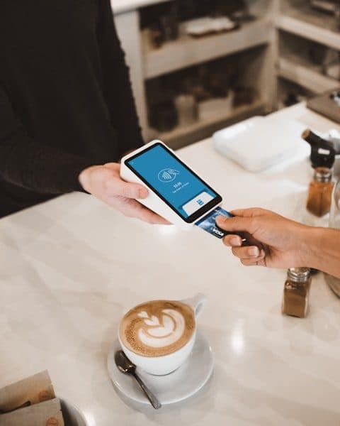 Handheld card terminal held across a café counter while a customer inserts a chip card.