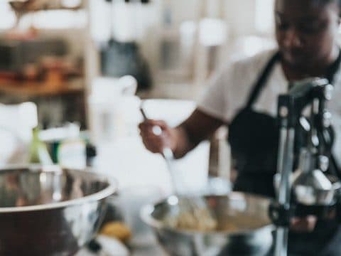 Chef plating food beside stainless mixing bowls on a busy commercial kitchen line.