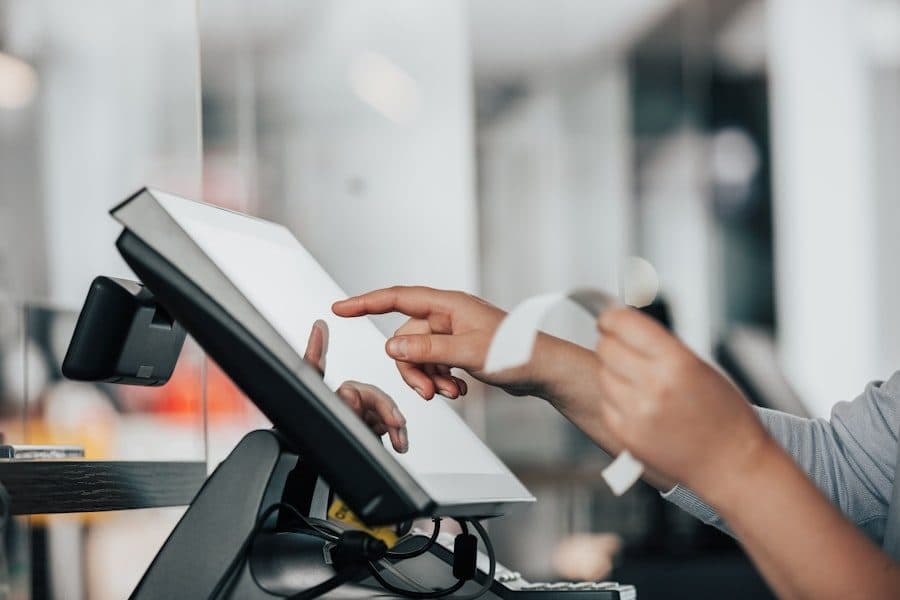 Countertop touchscreen POS terminal being tapped by a cashier as a receipt prints.