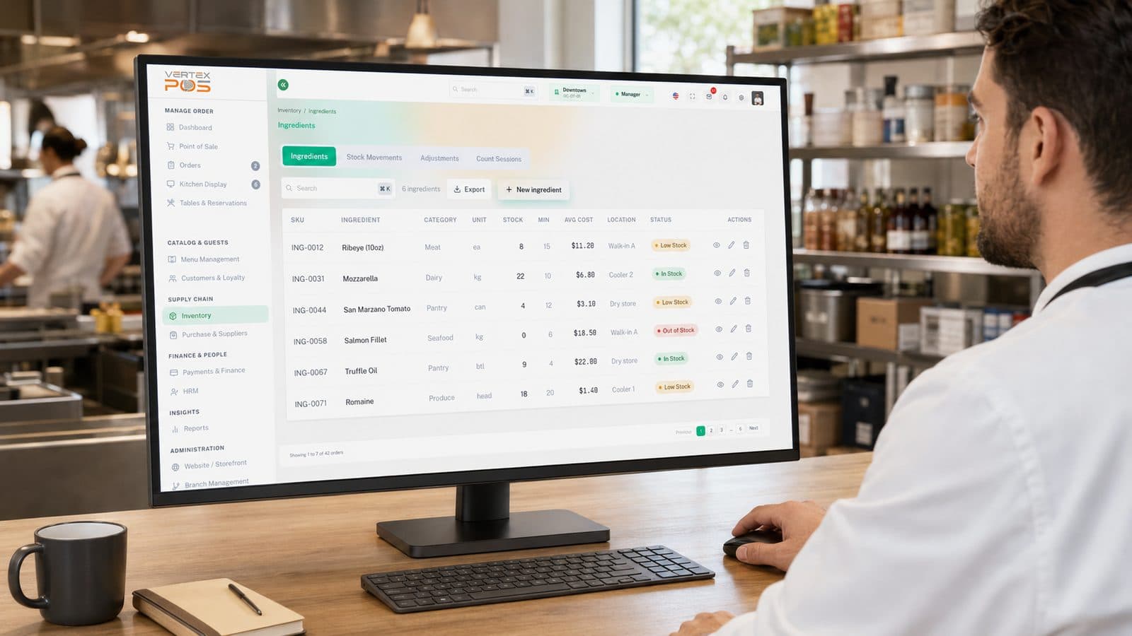 A chef reviews the Vertex POS Ingredients list on a desktop monitor in a restaurant kitchen, showing each ingredient's SKU, unit, stock on hand, minimum level, average cost, storage location and stock status.